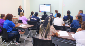 A group of people attending a training session in a classroom, facing a presentation screen.